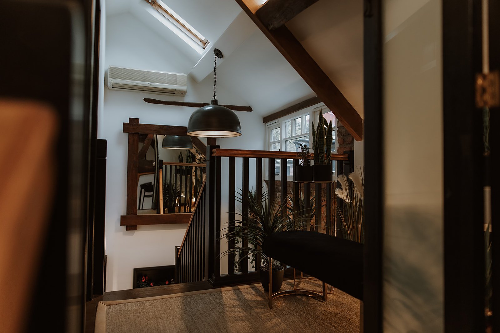 Interior of the upstairs at Salon XV in Oswestry, with a staircase, large windows, hanging pendant lights, and various plants.