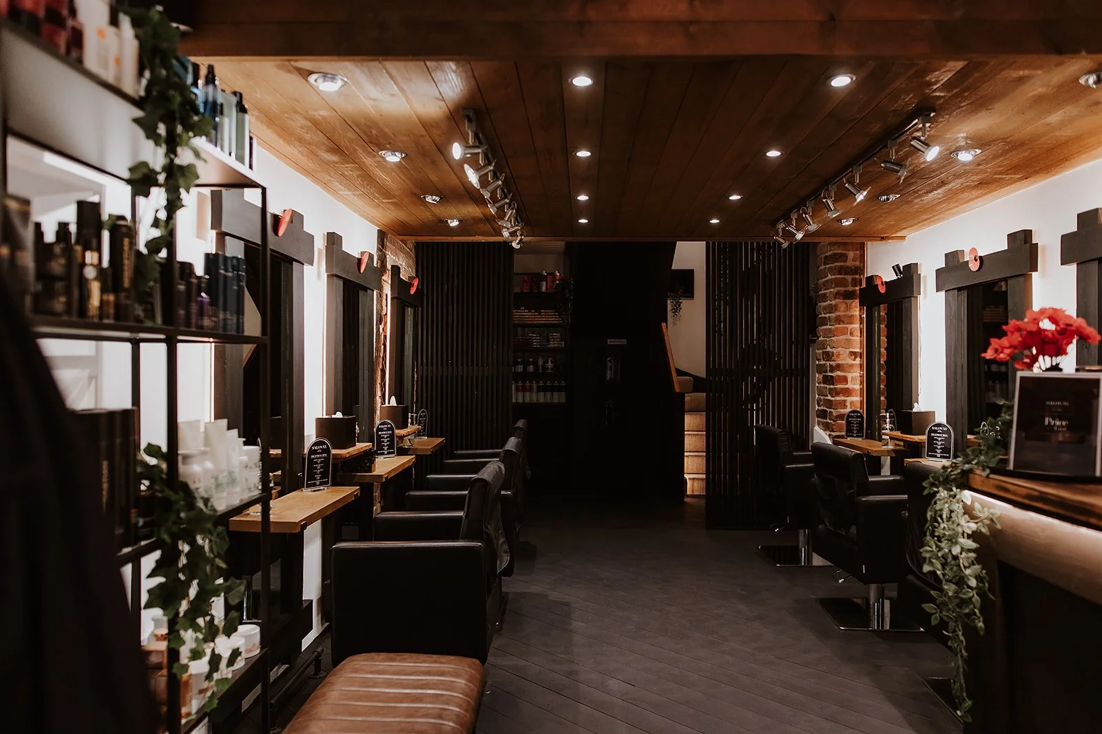 Welcoming interior with wooden ceiling, black chairs at wooden counters, brick accents, and soft lighting at Salon XV on Beatrice Street in Oswestry.