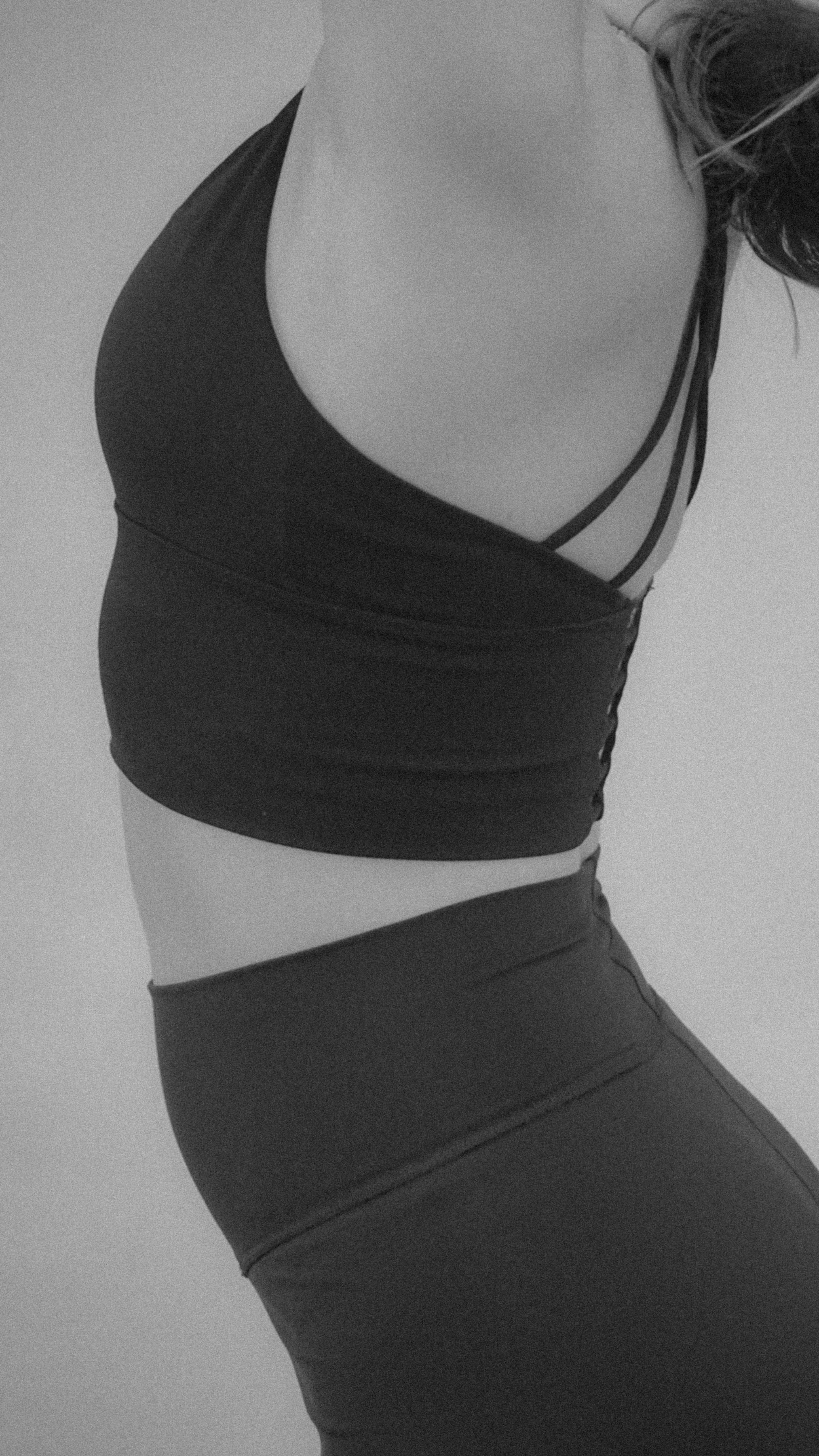 A black and white photo of a person in athletic wear, showing their torso, with a focus on their waist and chest, wearing a sports bra and leggings.
