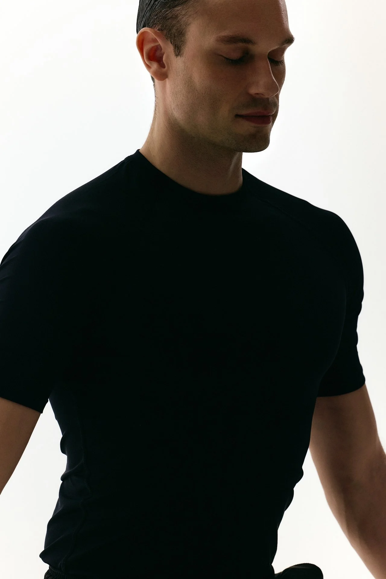 A man in a black t-shirt with his eyes closed, facing slightly downward against a plain white background.
