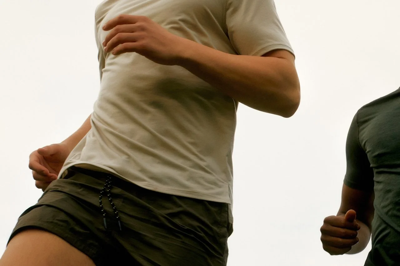 Lower bodies of two people running outdoors around an overcast sky.