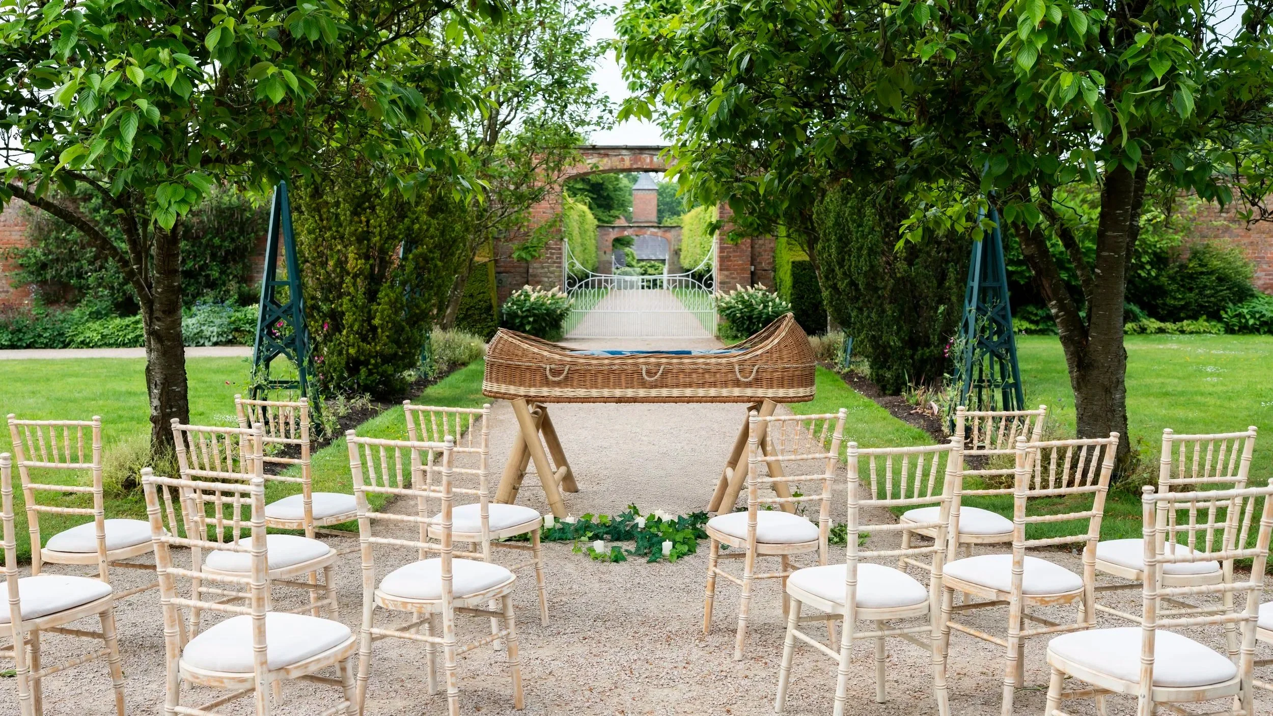 A group of empty chairs in front of a coffin on trestles in a garden
