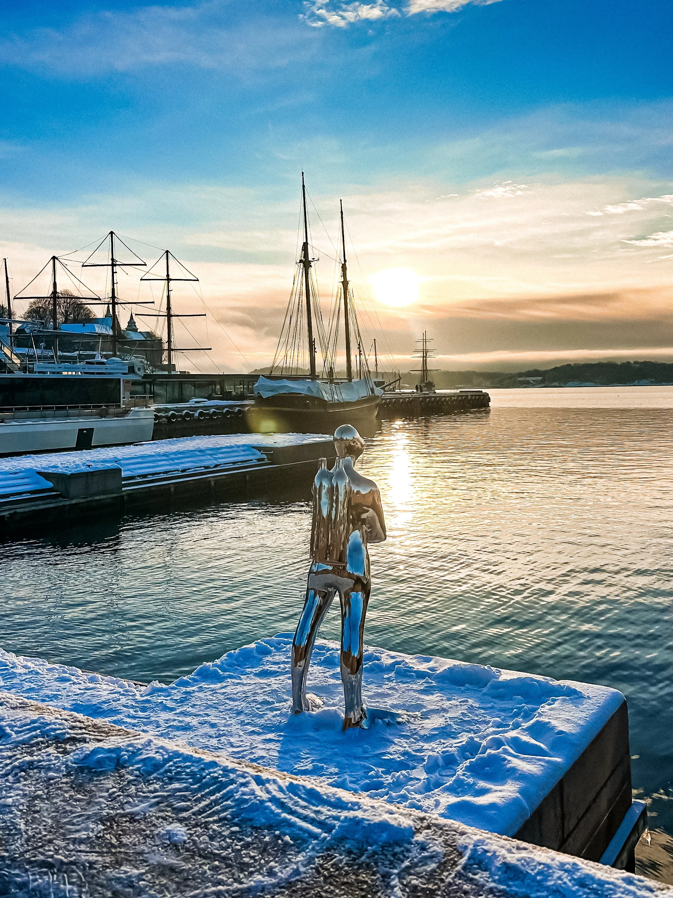 wander-senses-norway-oslo-akker-brygge-harbor-covered-with-snow-silver-sculpture-of-a-man.png