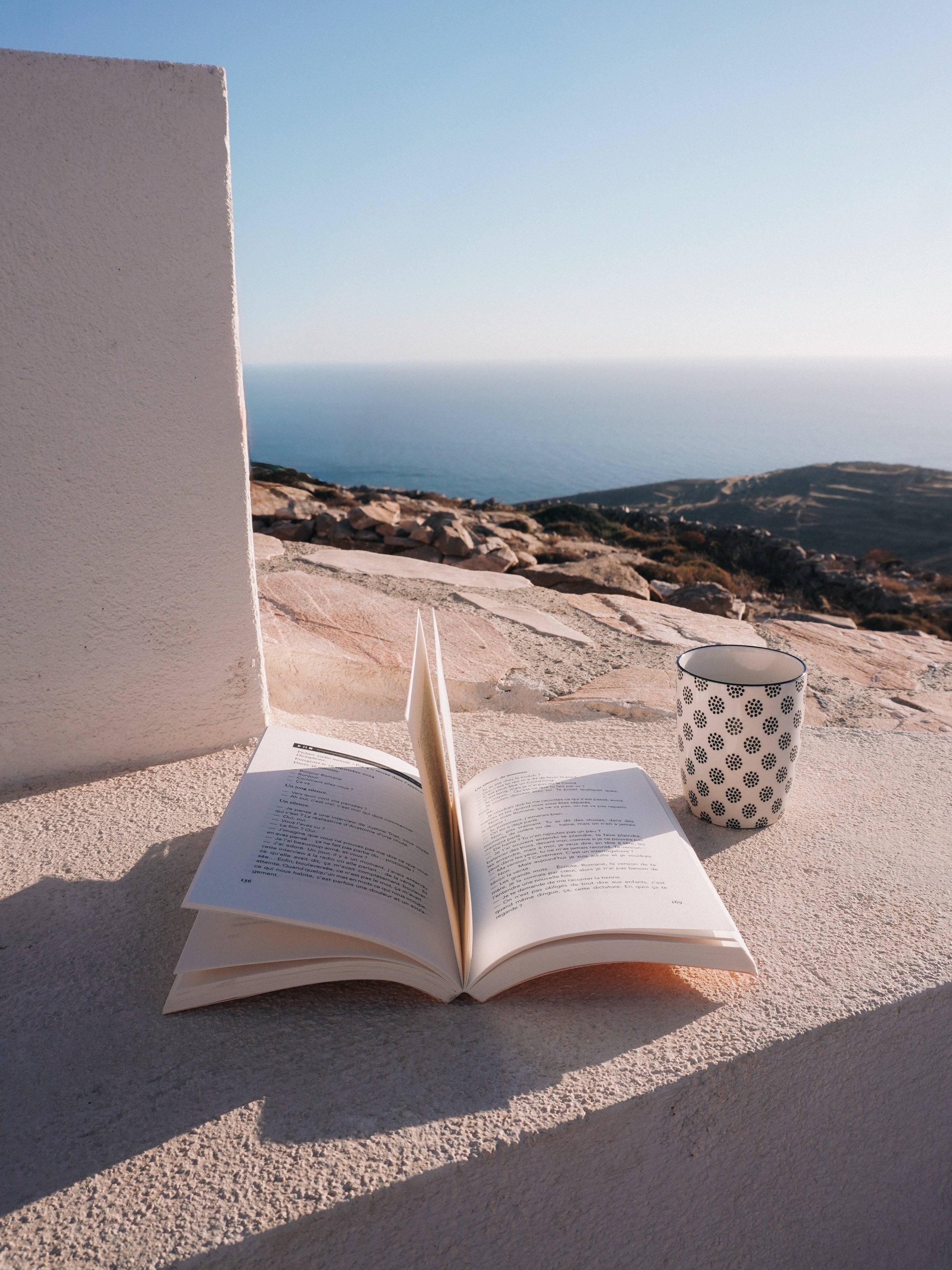 a book and a cup of coffe with a blue sea view in Greece