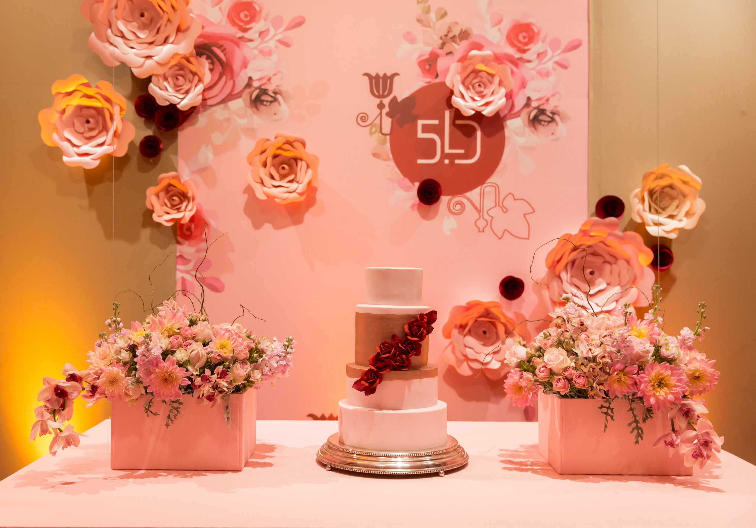 O símbolo fazendo uma união das iniciais da aniversariante LD com os seus 50 anos, versão 5.0.&nbsp;Aplicado em todo o material gráfico, aqui está impresso em tecido com a aplicação de flores em papel.