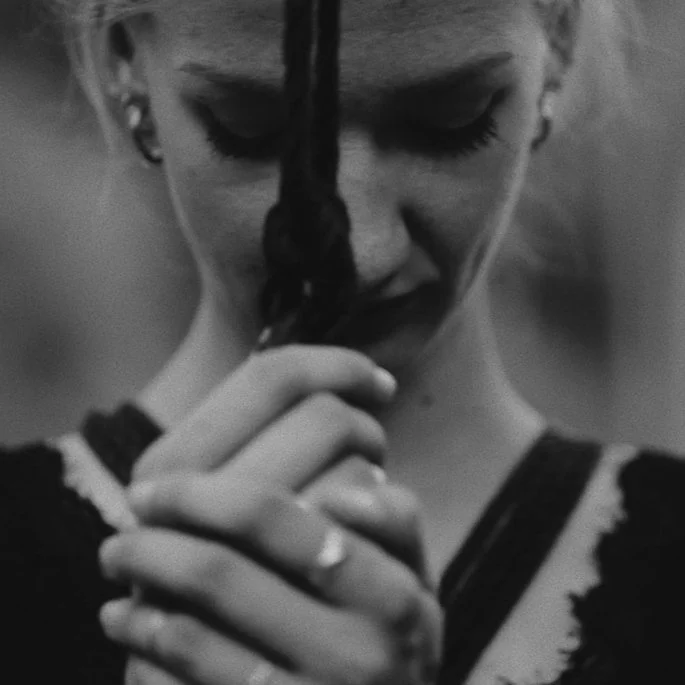 A hand reaching to pick up a pink lip gloss from a clear acrylic display with various lip glosses and nail polishes, some labeled '4SHAVE' and others with different colors.