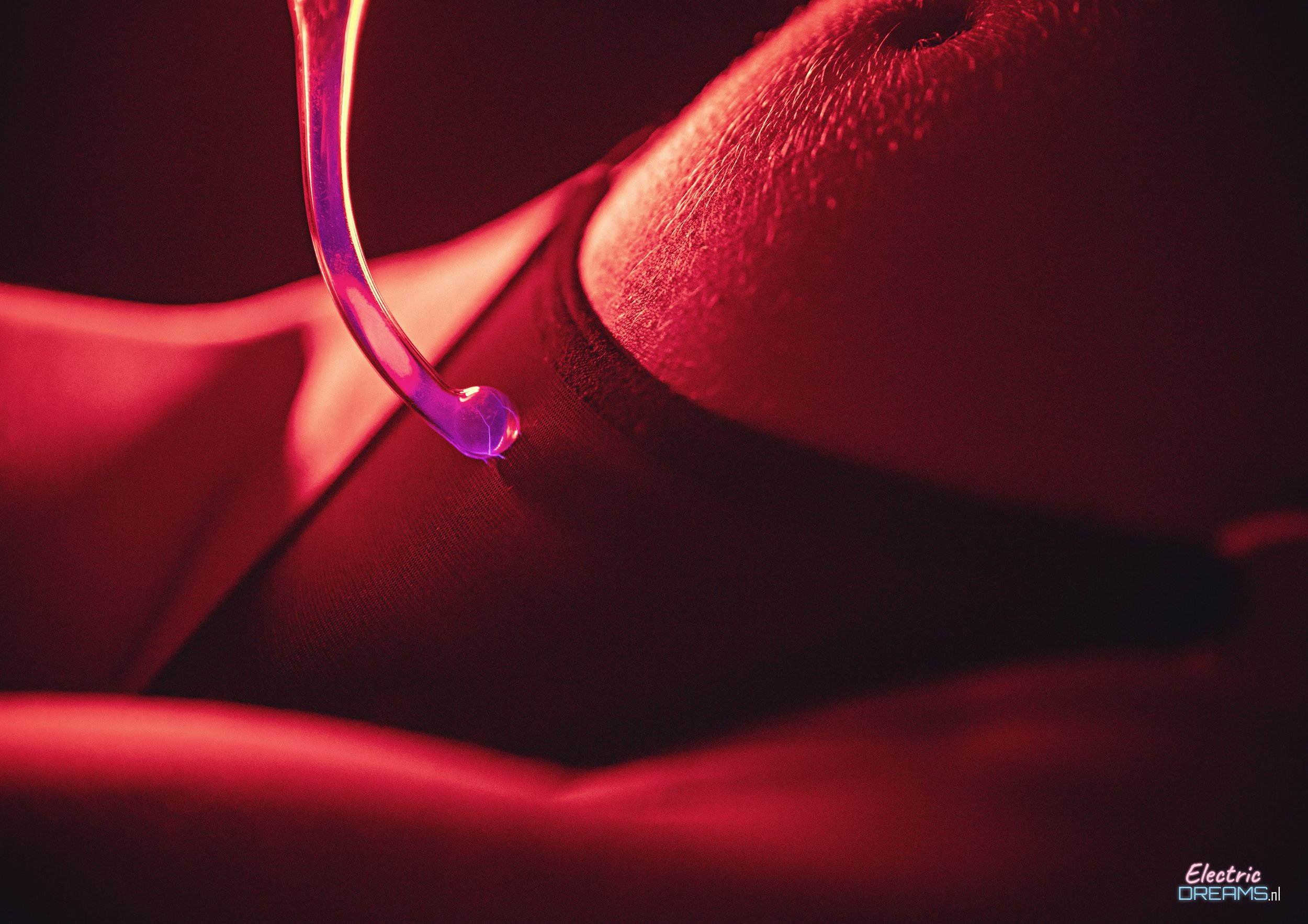 Close-up of a person receiving a tattoo from a tattoo artist using a purple tattoo needle, with red lighting highlighting the scene and a focus on the detail of the skin and needle.