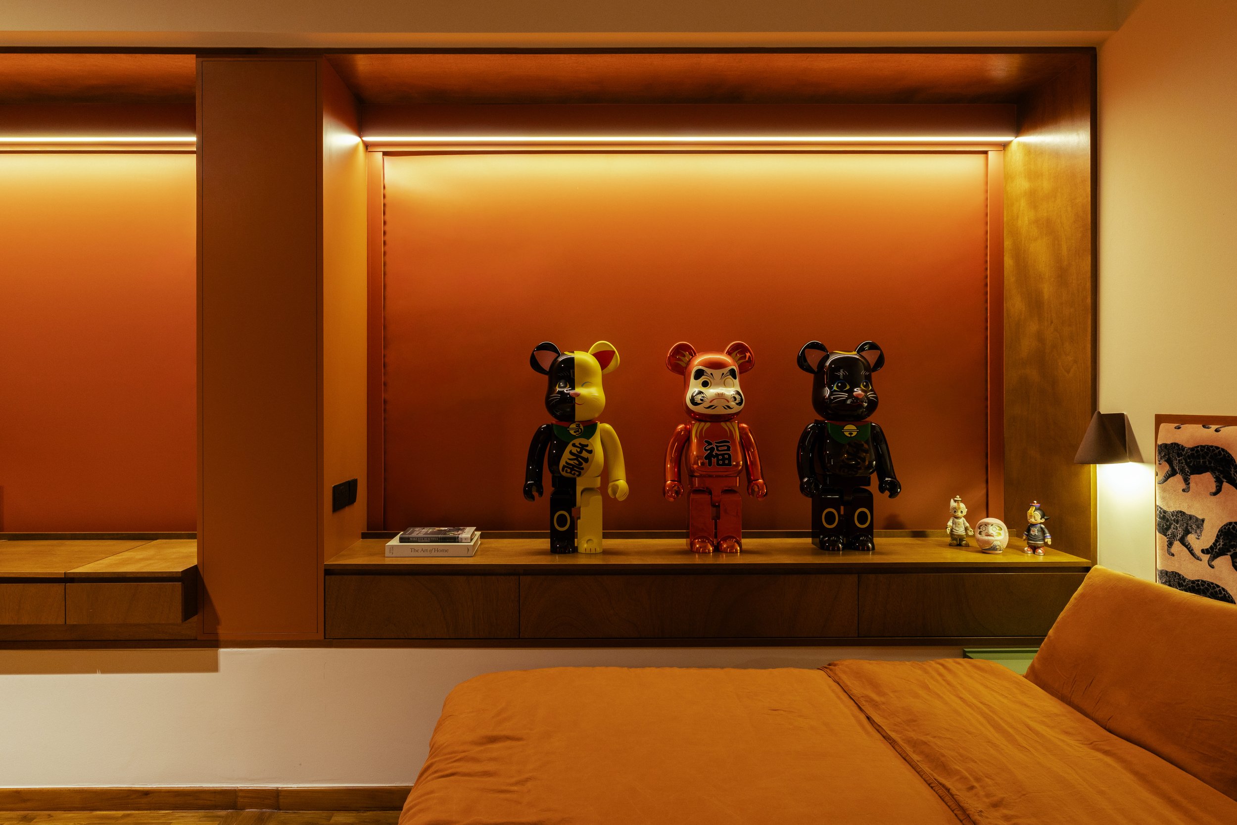 Decorative display of three colorful bear figurines on a wooden shelf against a warm-toned wood-paneled wall. Additional small decorations and books are also visible on the shelf.