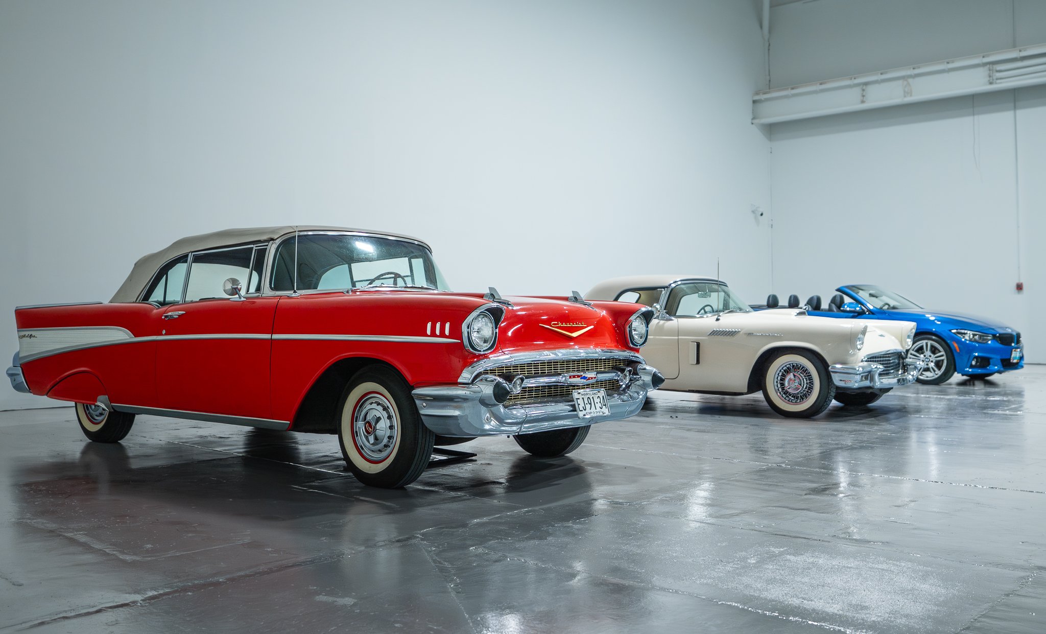 A person in a museum looking at a collection of classic and luxury cars displayed on elevated platforms inside a spacious, well-lit industrial-style building.