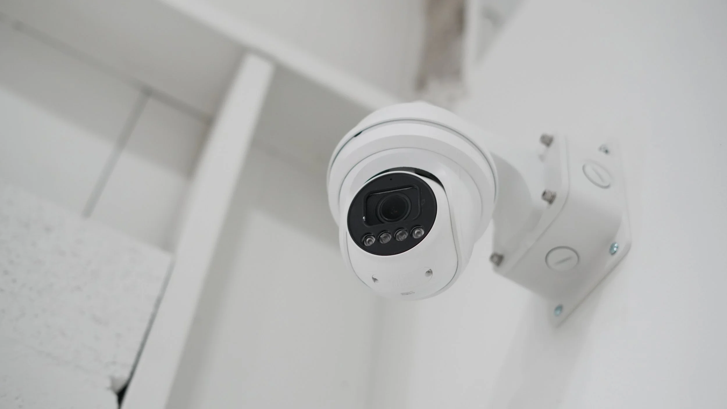 Close-up of a vintage outdoor security light fixture mounted on a wall with brown wooden siding, viewed from below against a blue sky.
