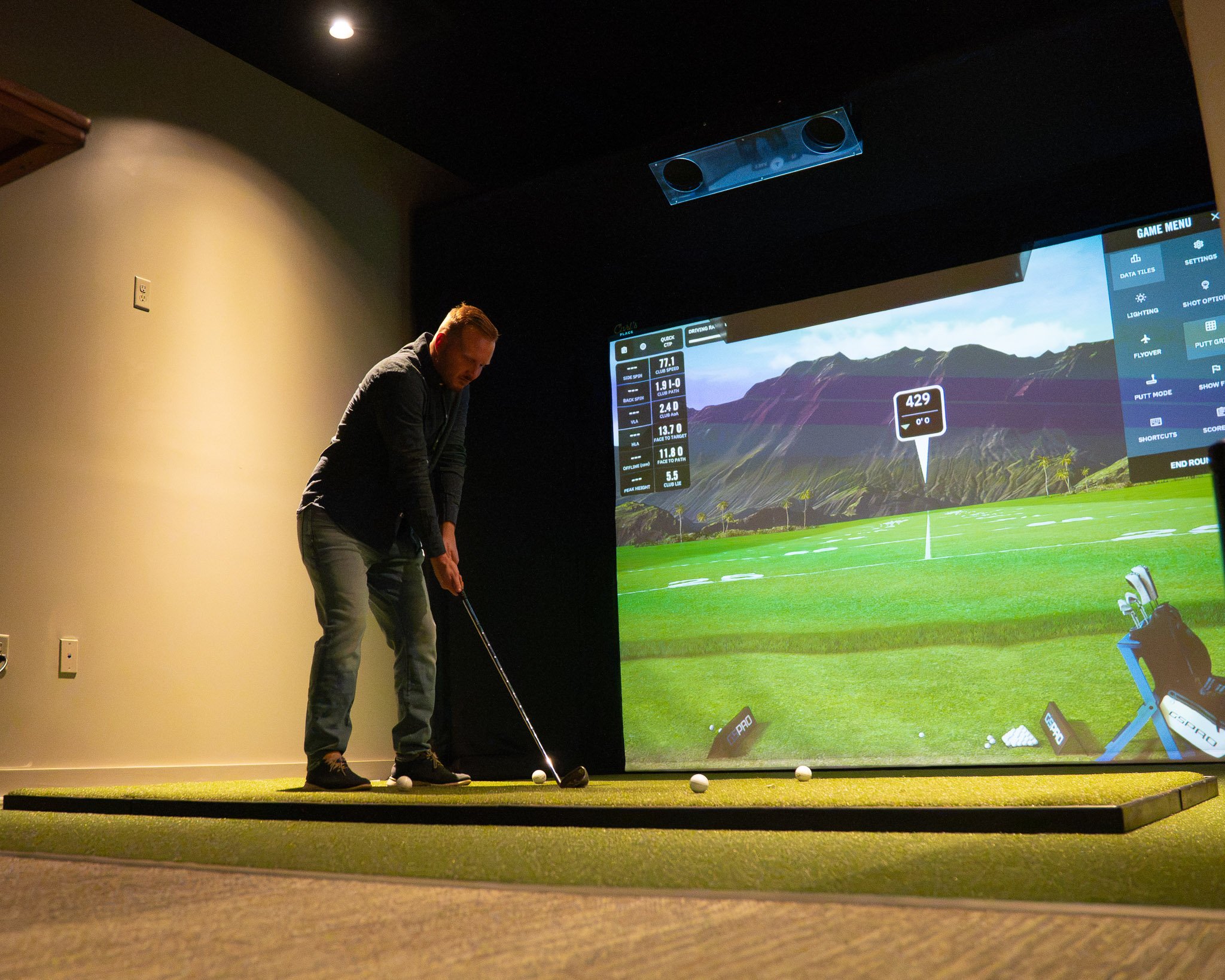 People playing indoor golf at a golf simulation center with large screen displays showing virtual golf courses.