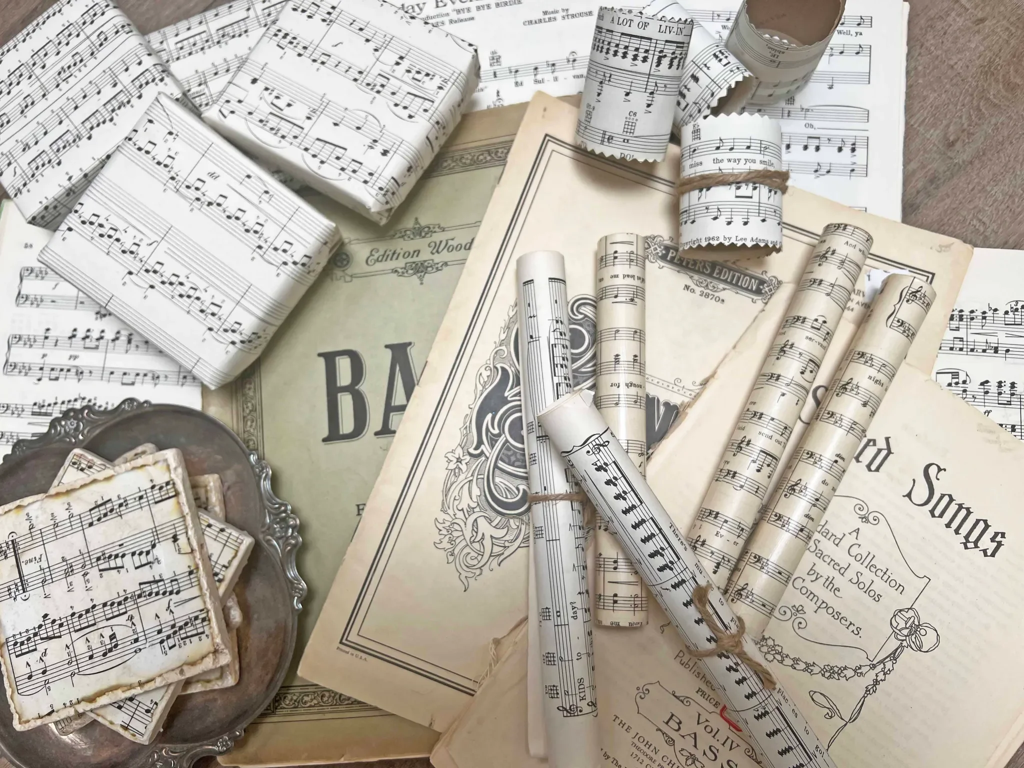 A collection of vintage sheet music, some rolled and some flat, on top of old sheet music books and a decorative tray.