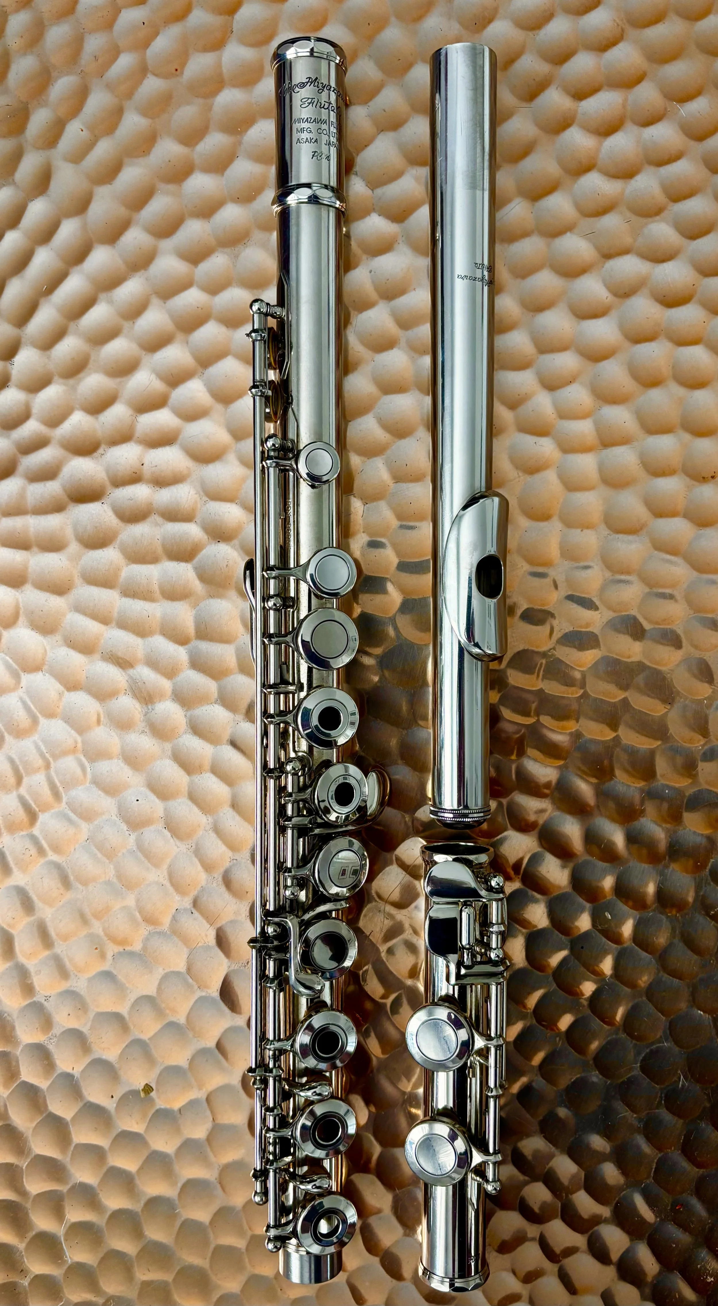 A silver flute disassembled into three parts on a textured beige surface.