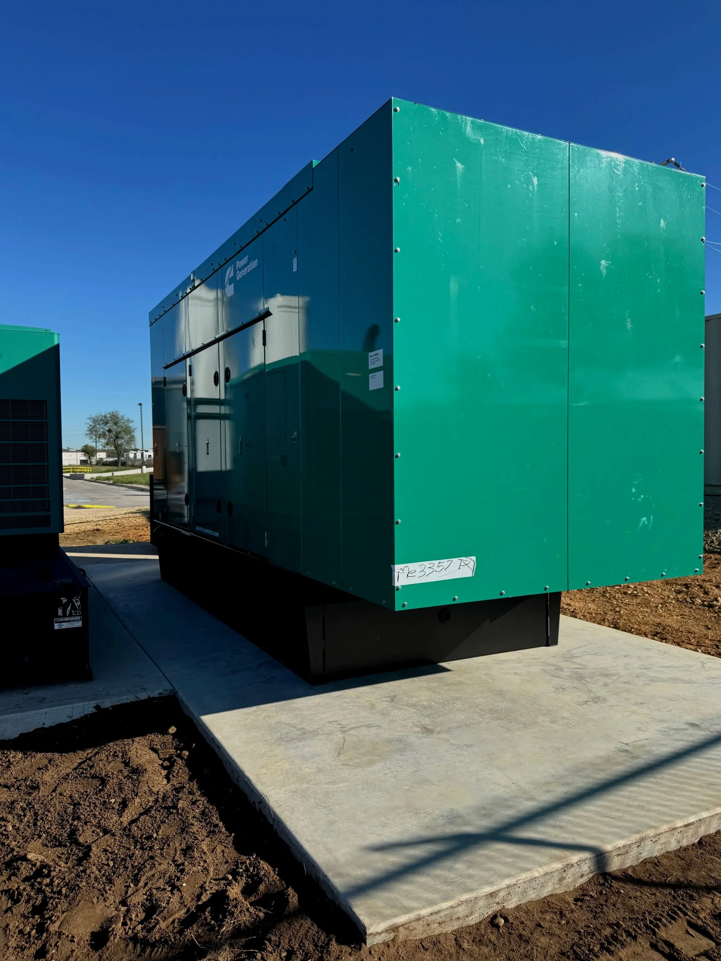 Green electrical generator unit placed on a concrete pad outside under a clear blue sky.