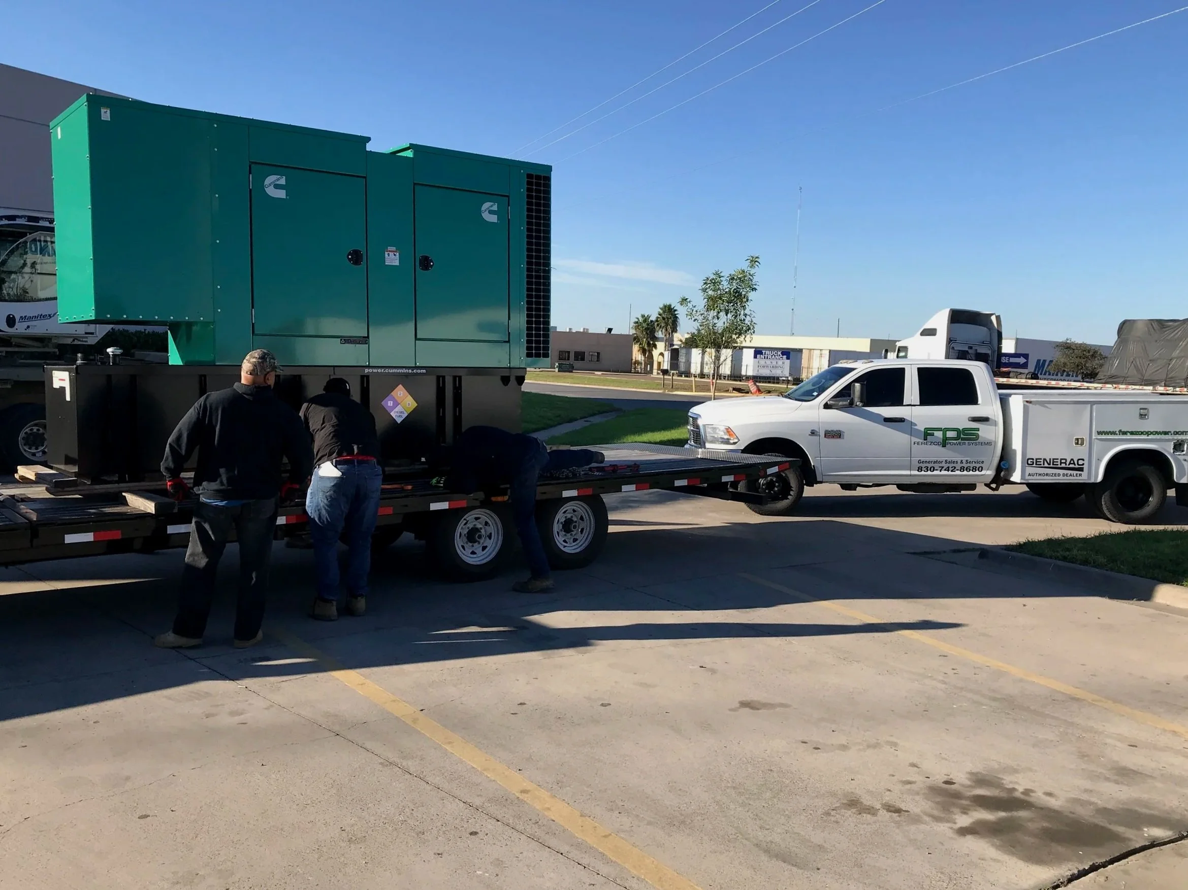 Workers loading or unloading equipment from a trailer truck in a parking lot with a large green generator and utility vehicle nearby.