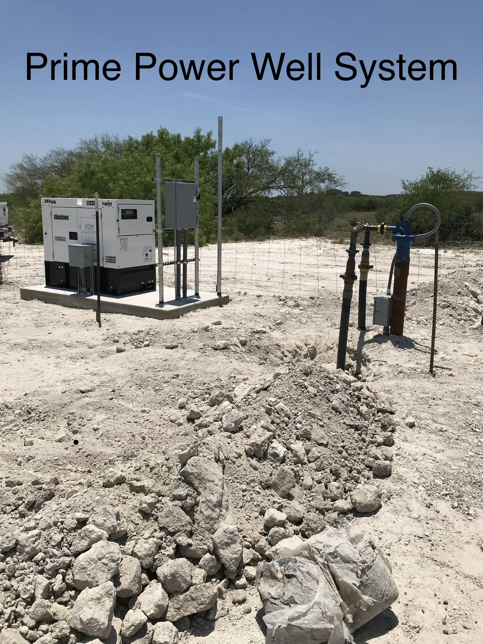 A solar-powered well system with piping and electrical equipment set up in a barren, rocky landscape with sparse trees and a clear blue sky.