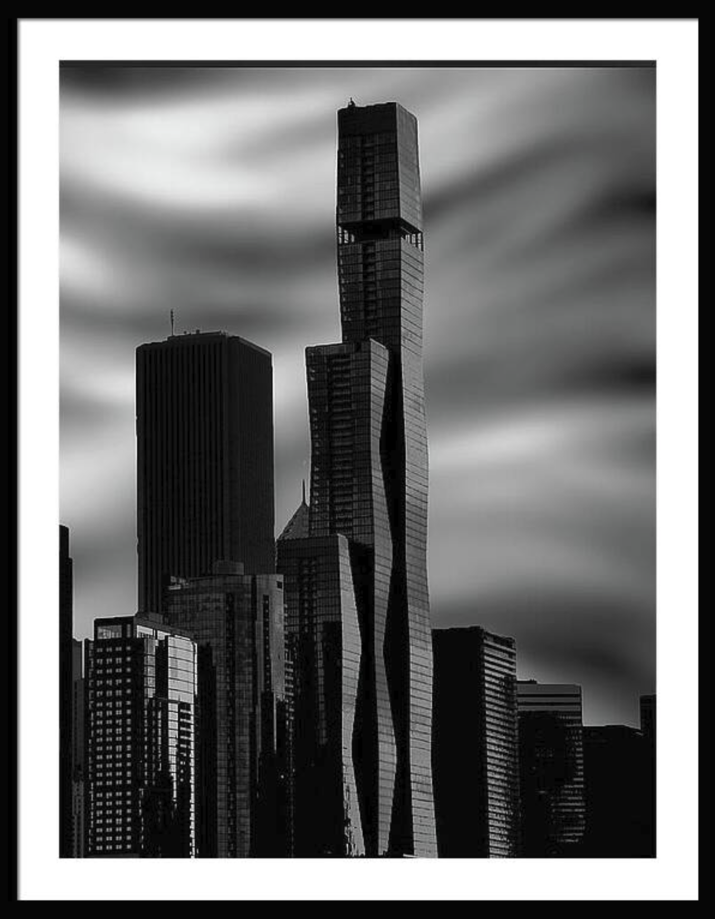 Black and white photo of modern skyscrapers with clouds in the sky.