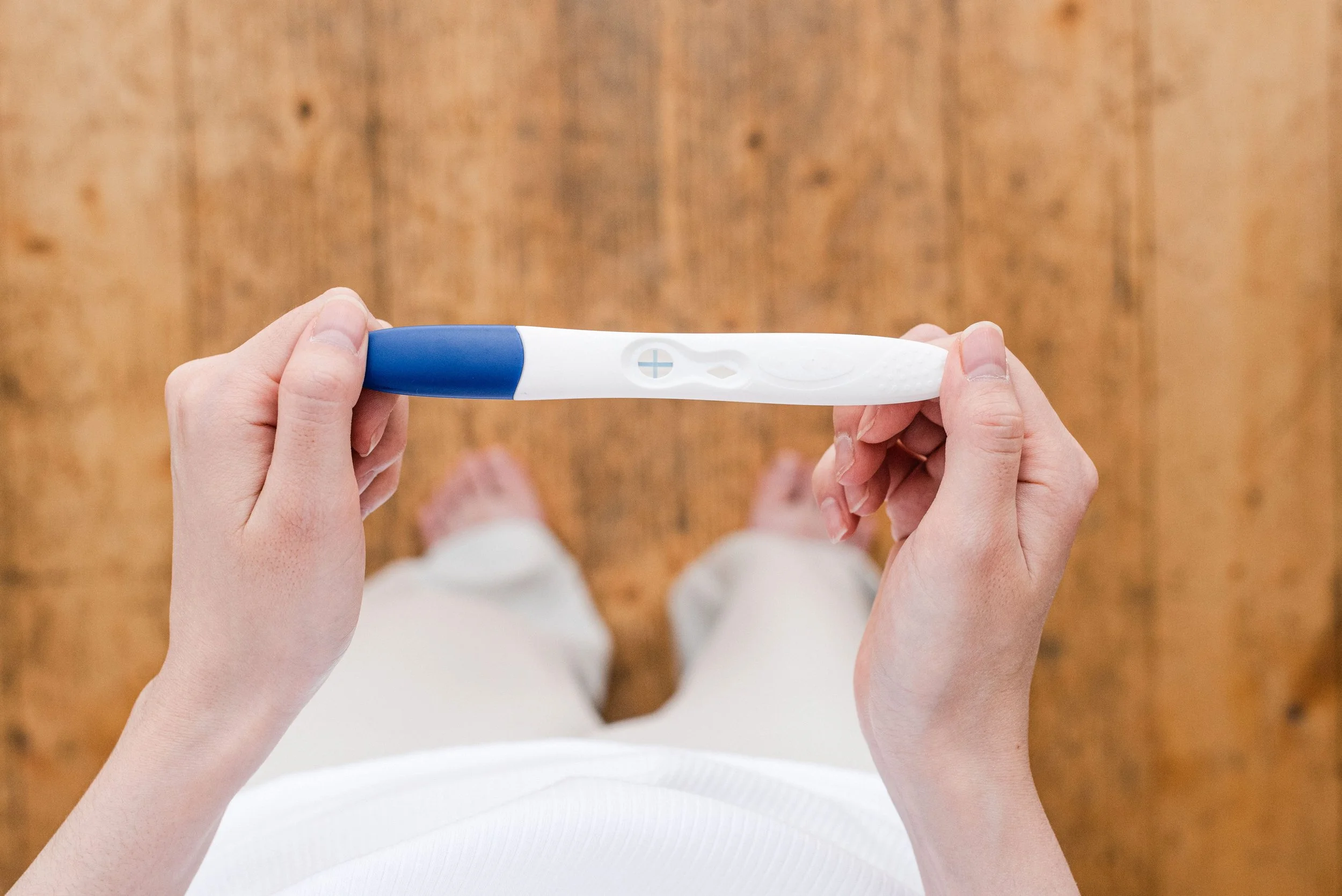 woman stands wood floor looking at positive pregnancy test in her hands