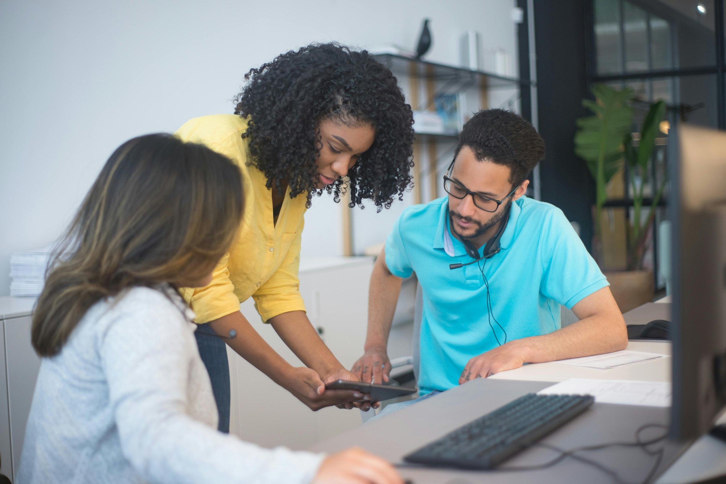 Three coworkers in a modern office collaborating around a tablet device.