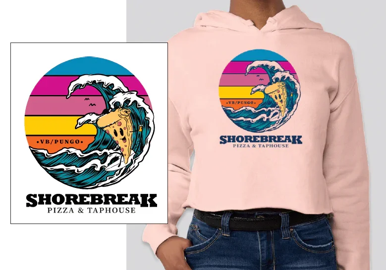 Pink hoodie featuring a colorful graphic of a surf wave with a slice of pizza in the center, and the text 'SHOREBREAK PIZZA & TAPHOUSE' beneath the graphic.