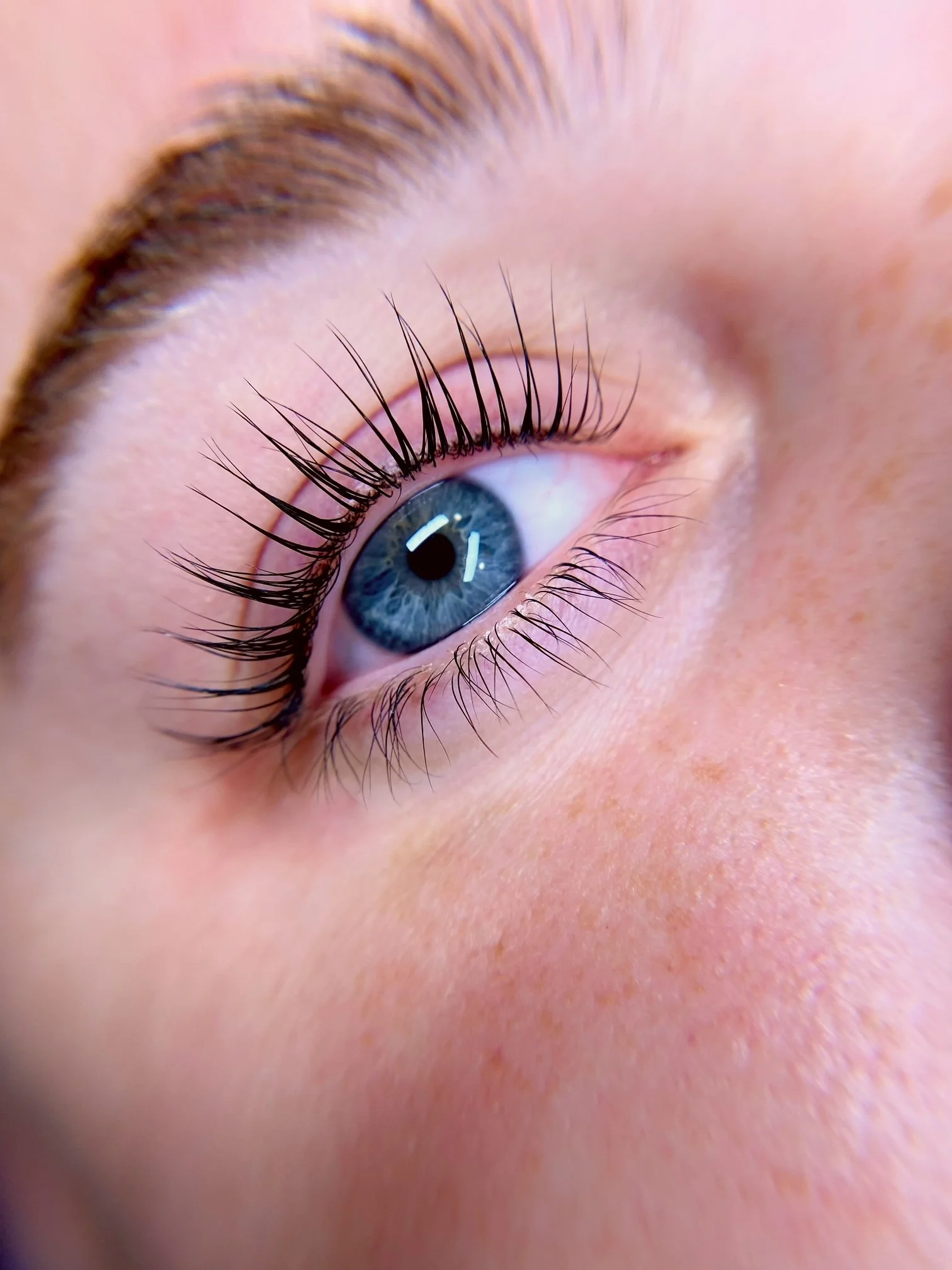Close-up of a blue eye with long, dark eyelashes and lightly freckled skin surrounding it.