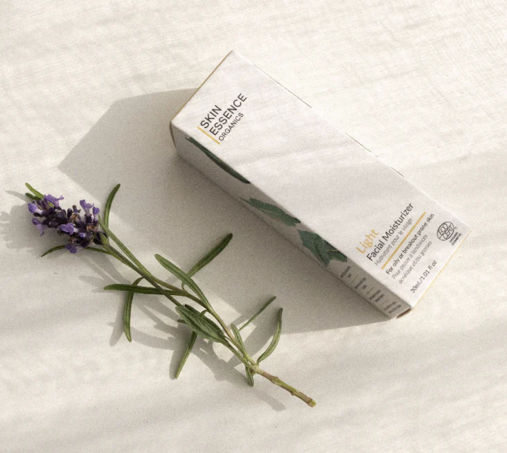 A box of Skin Essence Organics Light Facial Moisturizer and a sprig of lavender on a white surface.