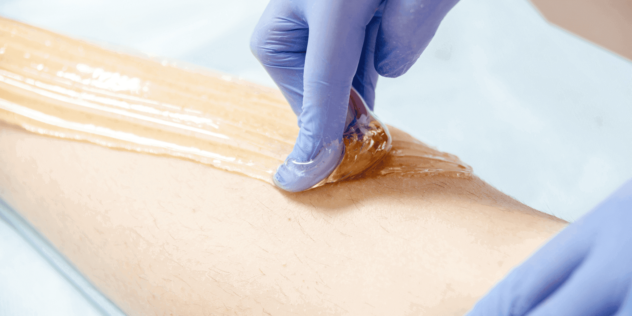 Close-up of a person wearing blue gloves applying wax strip to remove hair from leg.