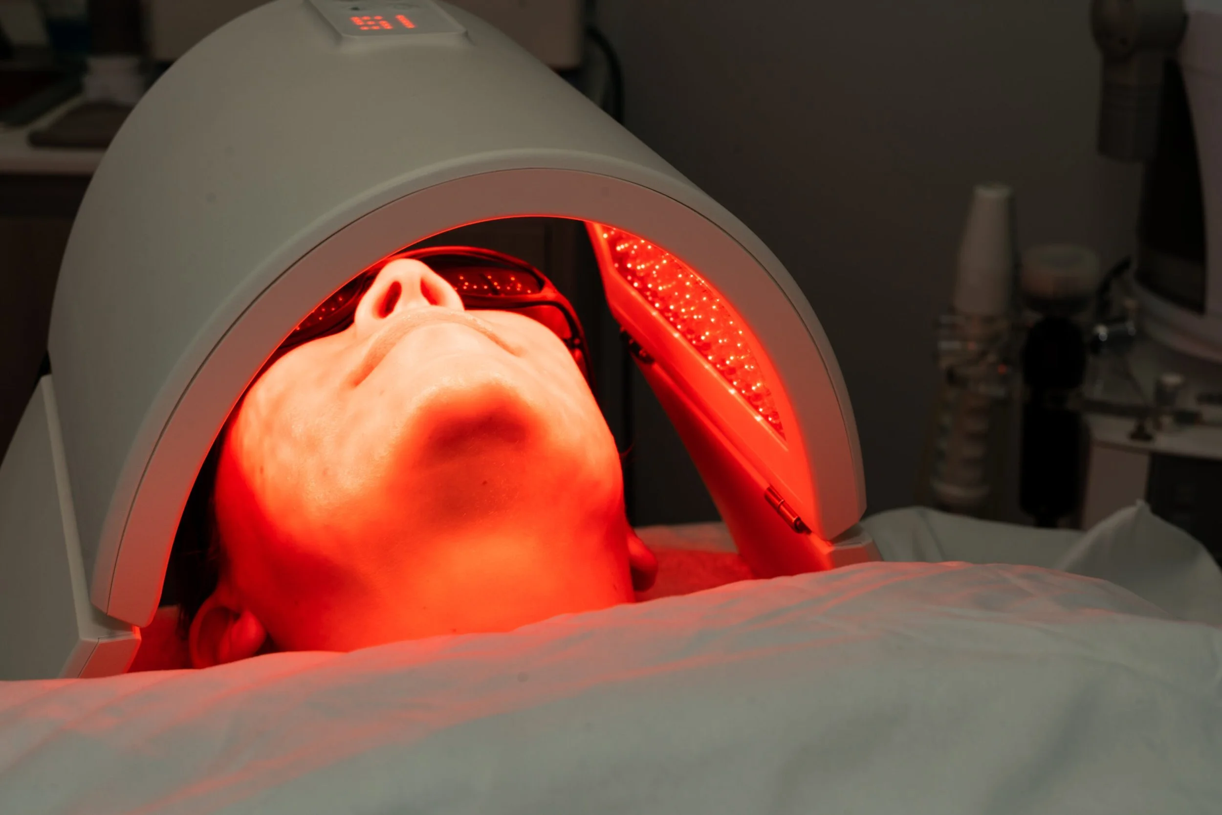 Person undergoing a red light therapy treatment with their face exposed inside a specialized radiator-like machine