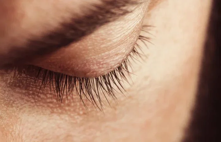 Close-up of a closed eye with long eyelashes and smooth skin.