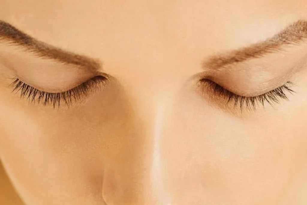 Close-up of a person's face with eyes closed, showing detailed eyelashes, eyebrows, and smooth skin.