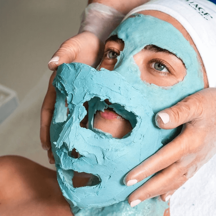 Person wearing a white headband and a blue facial mask, holding a matching cut-out mask in front of their face, exposing eyes and part of face.