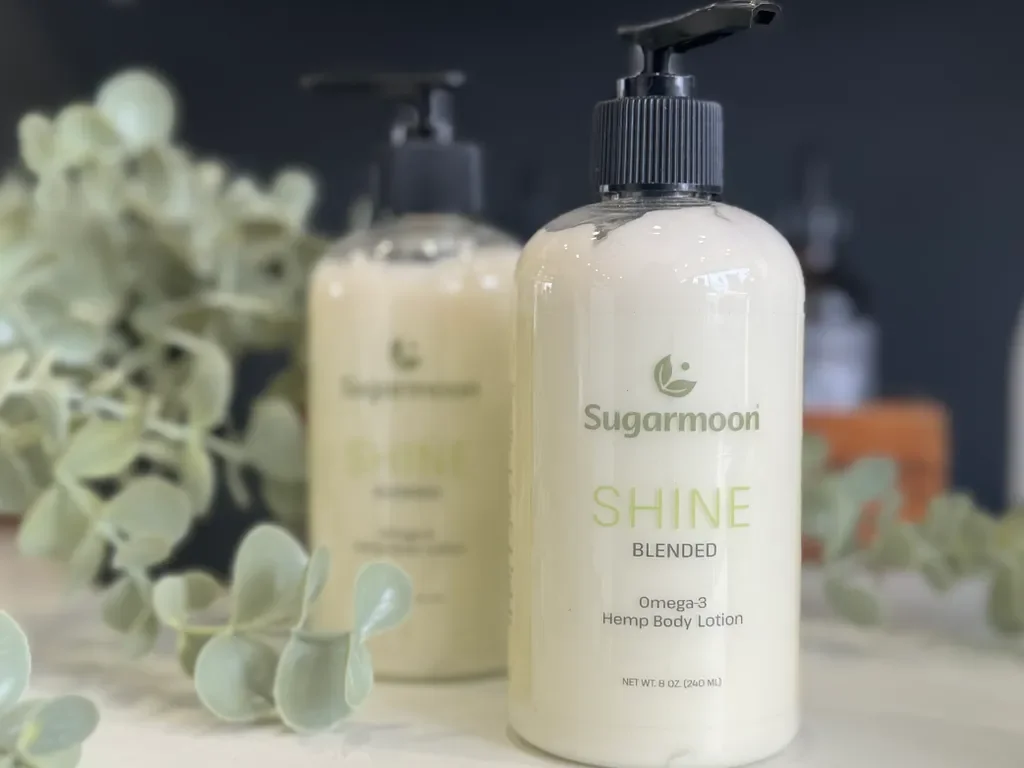 A bottle of Sugarmoore Shine Blended Omega-3 Hemp Body Lotion with eucalyptus leaves around it