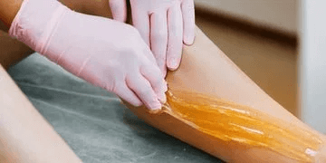 Person applying warm wax to a person's arm for hair removal.
