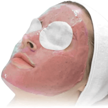 Person lying down with a facial mask and eye pads, wearing a white headband.