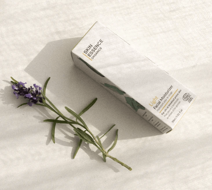 A box of Skin Essence Organics Light Facial Moisturizer and a sprig of lavender on a white surface.