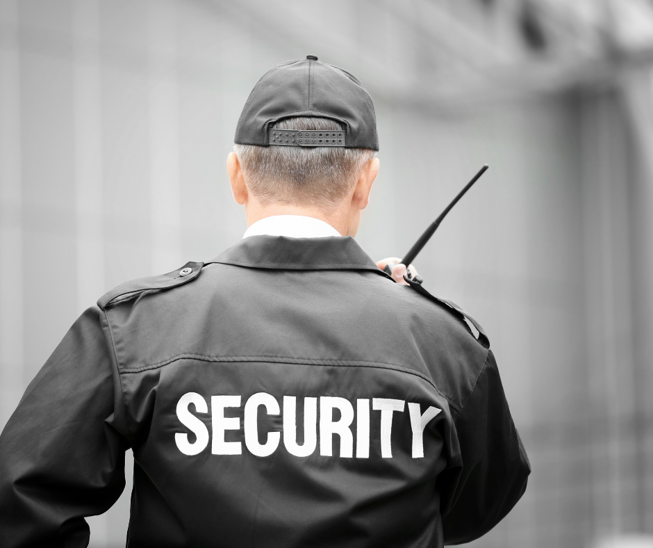 Back of a security guard in uniform with a walkie-talkie, wearing a cap and jacket with 'SECURITY' written on the back.
