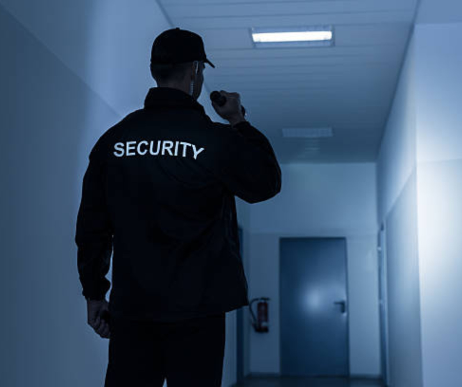 Security guard in black uniform holding a walkie-talkie, walking down a dimly lit hallway.