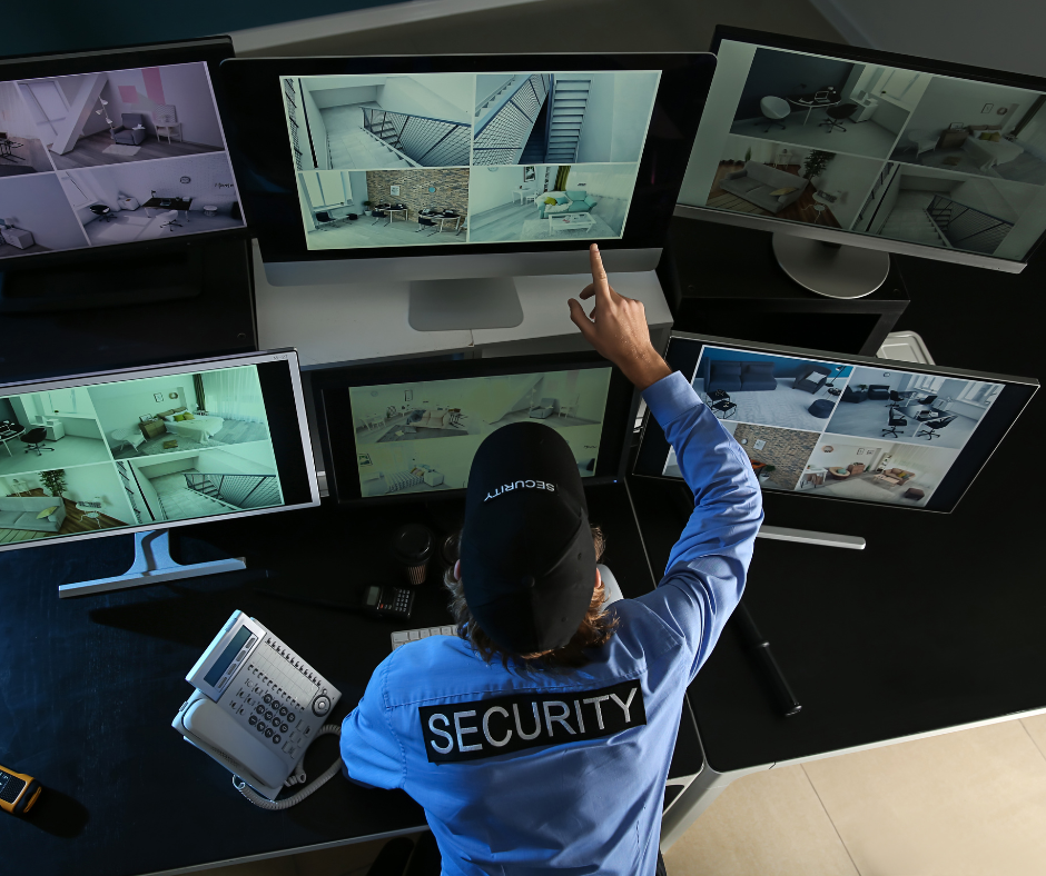 Security officer monitoring multiple surveillance screens showing various rooms.