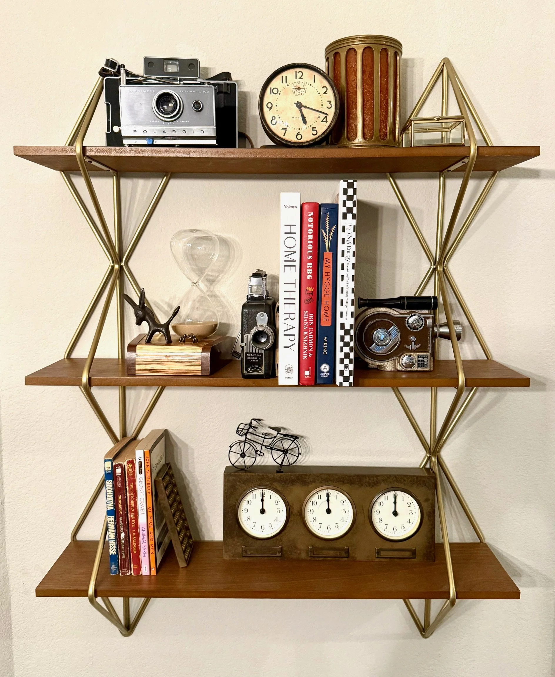 Wooden and gold metal wall shelf with vintage cameras, books, clocks, decorative items, and trinkets.