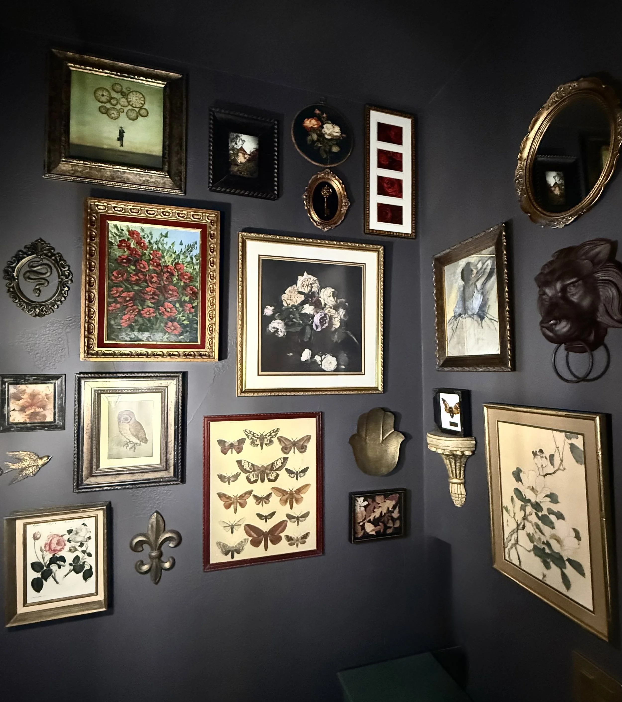 Wall decorated with various framed paintings and artwork, including flowers, birds, butterflies, and abstract designs, in a gallery or living space.