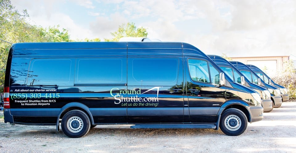 Black shuttle van with company branding parked with other similar vans in the background.