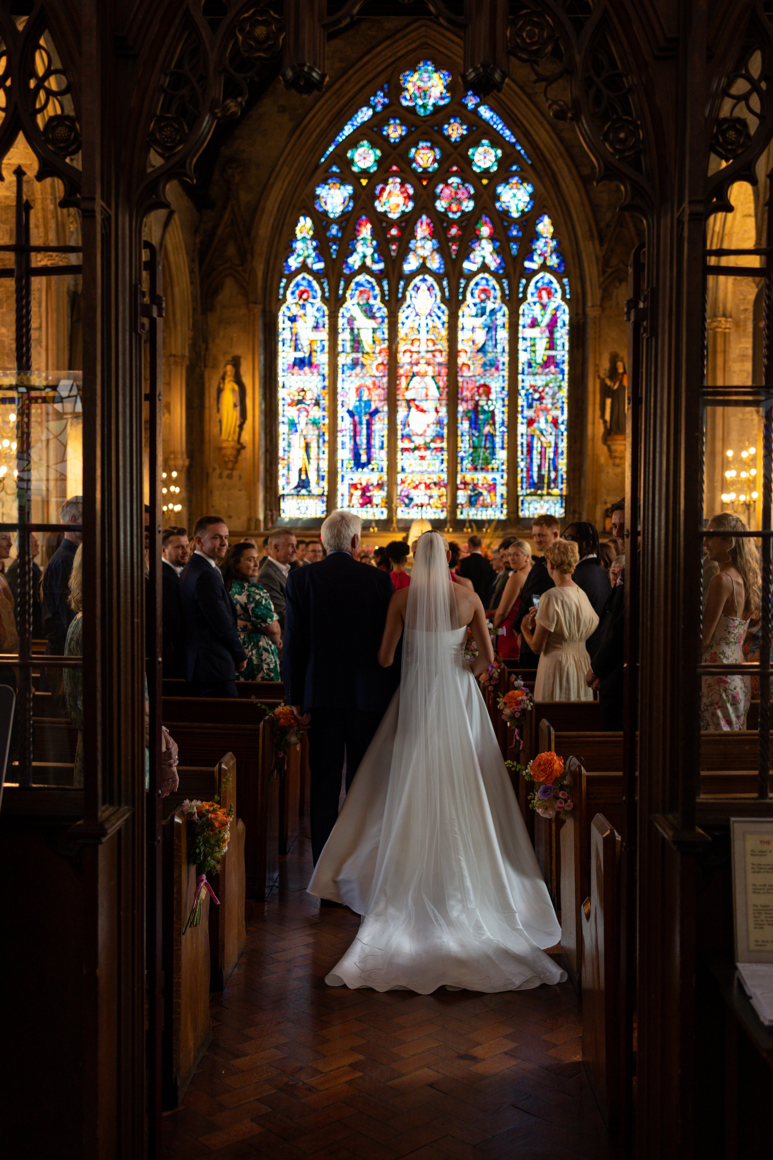 photo taken from behind as a bride walks down the aisle with her dad in a church