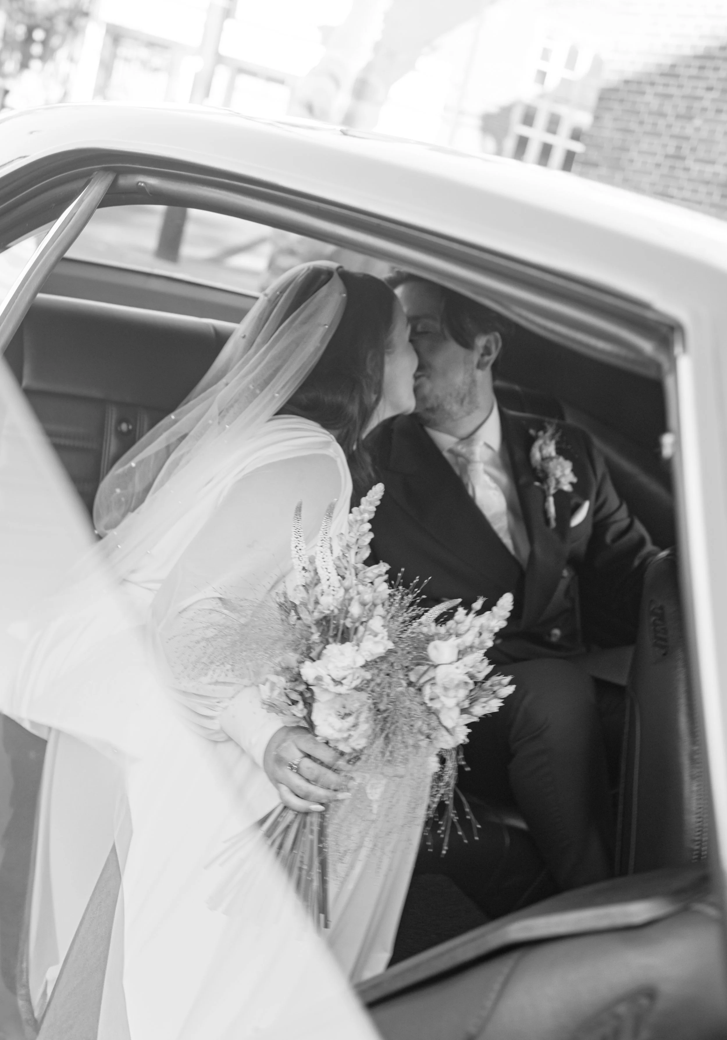 bride and groom kissing in the back of a wedding car