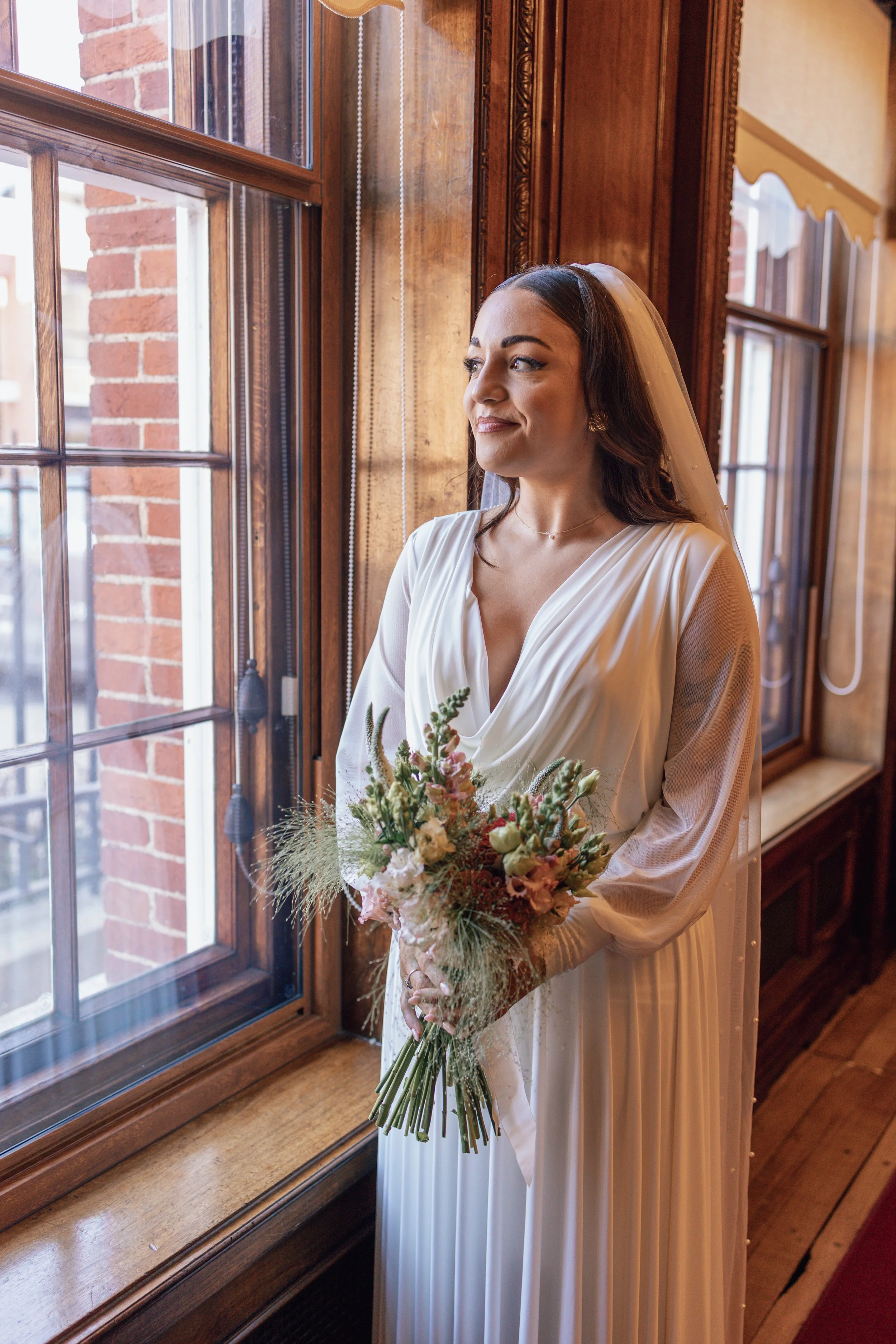portrait bride holding bouquet looking out of a window
