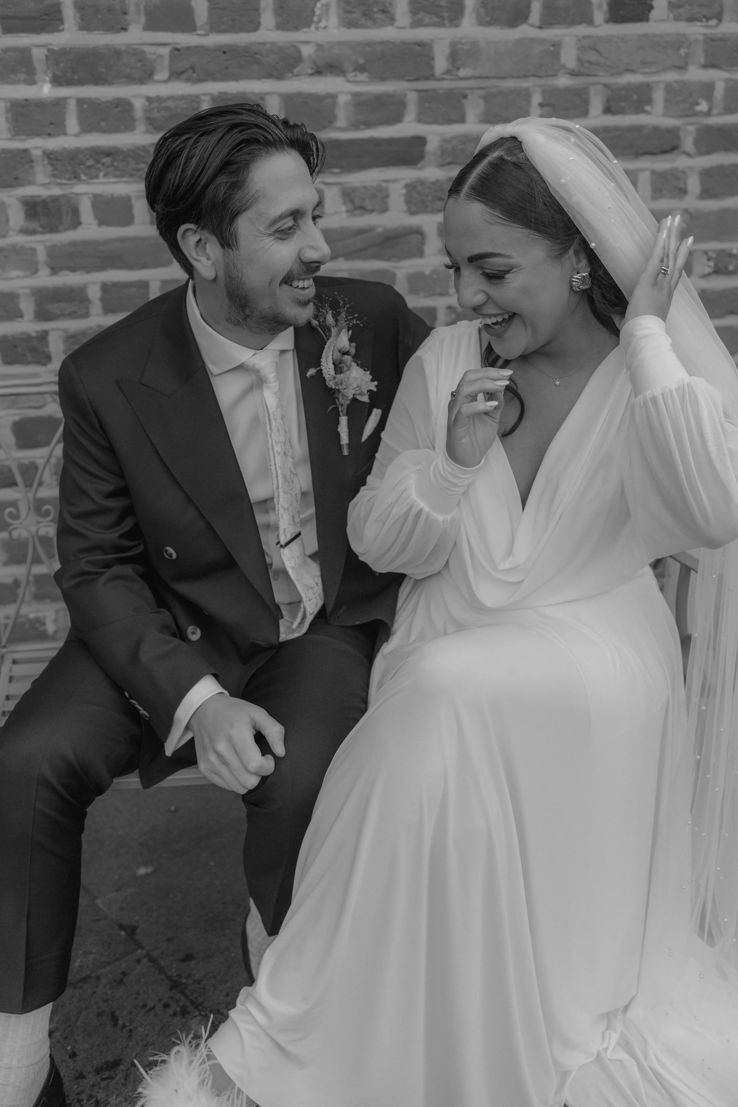 bride and groom giggling sat on a bench