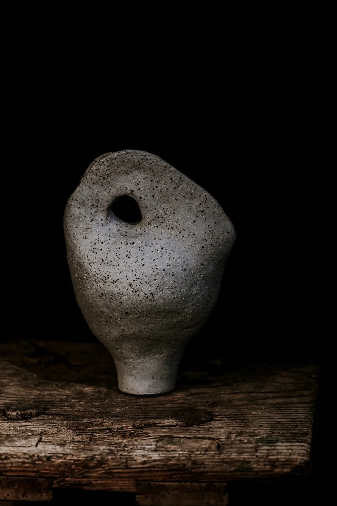 Eine skulpturartige Vase aus rauem Stein mit einer großen ovale Öffnung auf der Oberseite, auf einem alten Holzbrett gegen schwarzen Hintergrund.