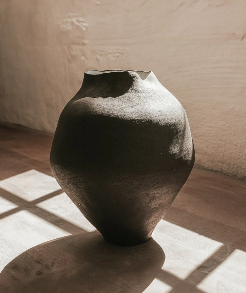 Schwarze, handgefertigte Keramikvase mit abgerundeter Form, Schatten an einer Wand. Verwendung in Innenräumen.