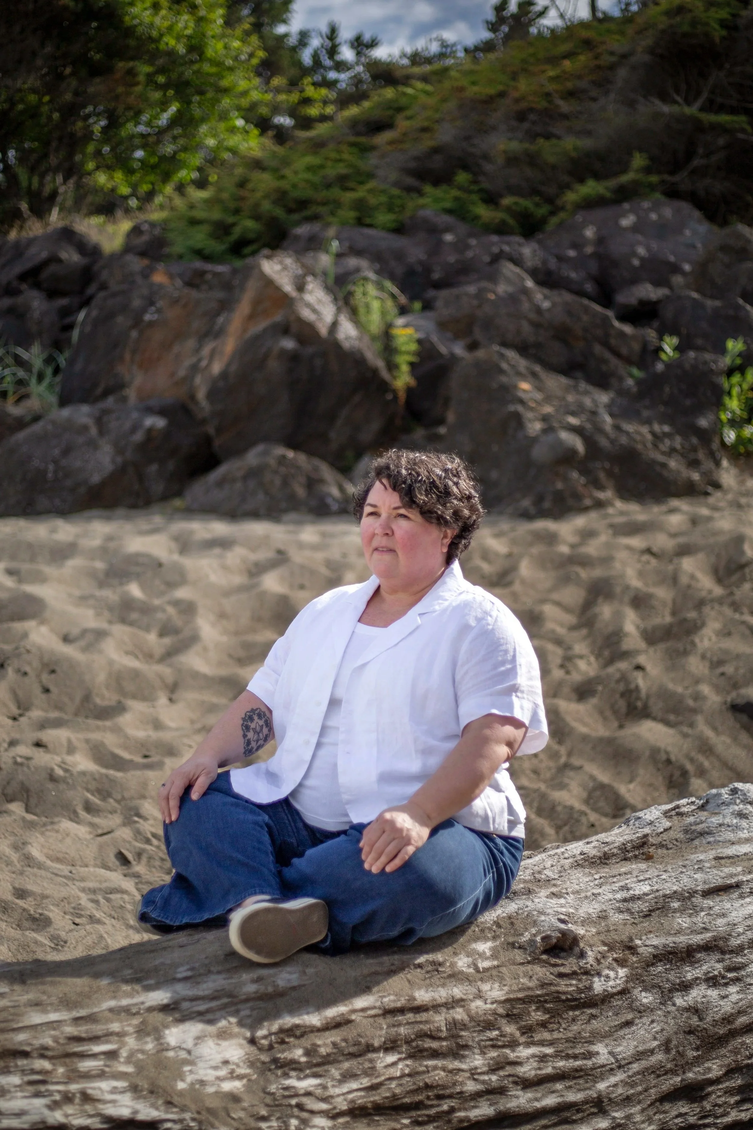 Heather Pierce, LMFT, sitting peacefully on driftwood at the beach, therapist for women and gender-expansive adults in Newport, Oregon