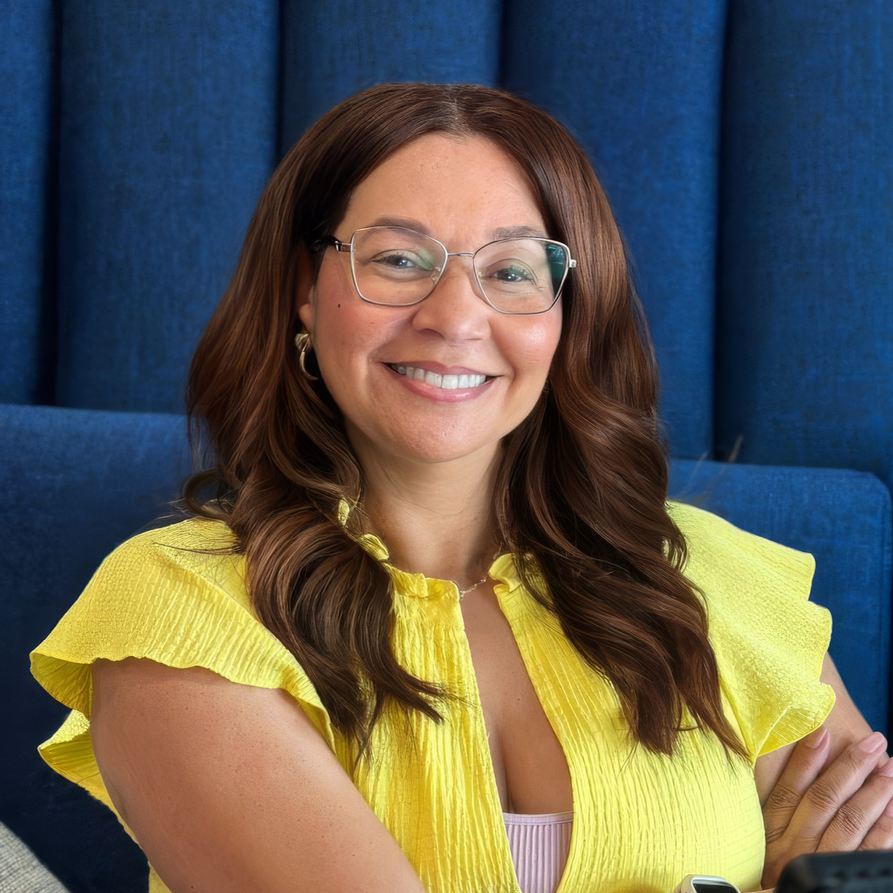 A woman with long black hair smiling, wearing a blue floral blouse, against a blue background.