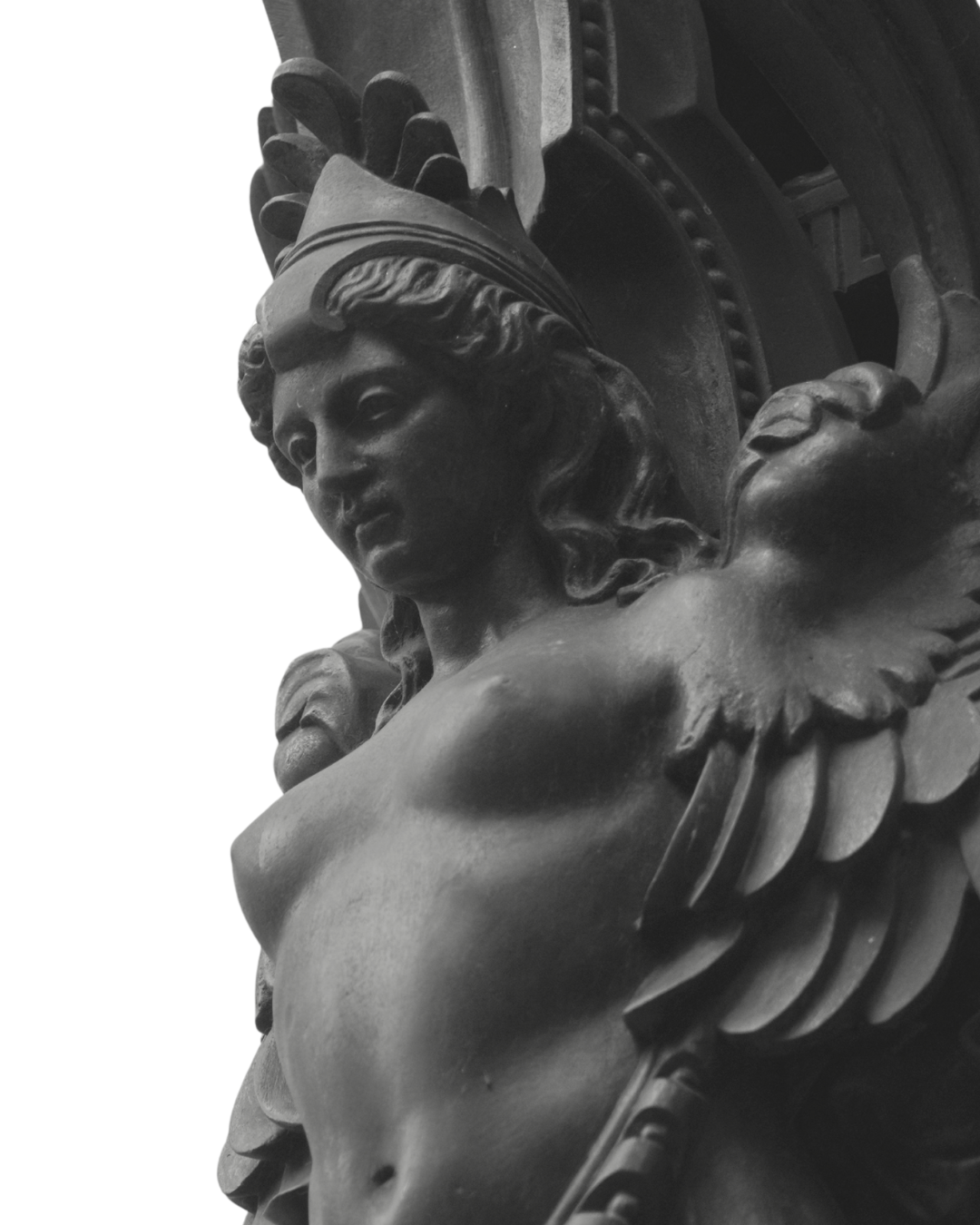 A close-up black and white photograph of a detailed sculpture of a woman with a headdress and wings, featuring classical artistic style.